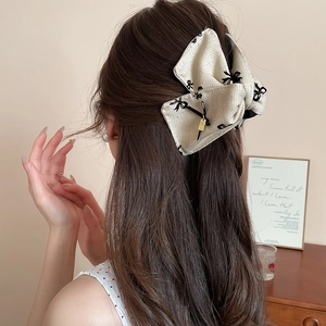 Detailed close-up of a cream-colored tweed bow hair claw clip with black floral print