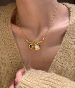Détail d'un collier pendentif oeil de tigre plaqué or 18K sur un pull en maille beige