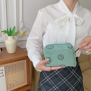 Detail of mint green corduroy makeup bag with smiley prints held by a hand