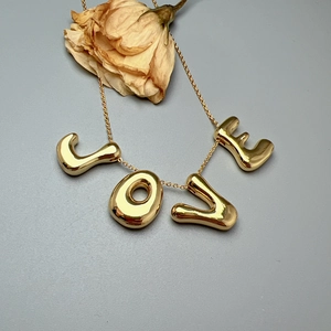 Golden stainless steel LOVE letter pendant necklace displayed with a dried rose on grey background