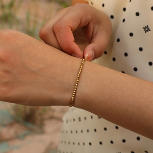 Detail of adjustable gold beaded bracelet with faceted metallic beads on wrist
