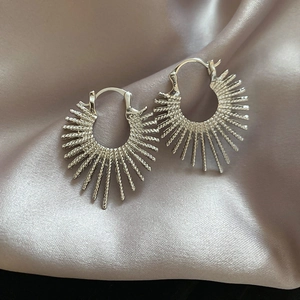 Detail of silver sunburst hoop earrings with irregular rays on elegant silk background