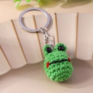 Handmade green crochet frog keychain with silver ring on a beige ceramic plate