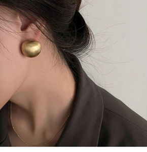 Close-up of large golden matte round stud earrings with brushed metallic texture detail