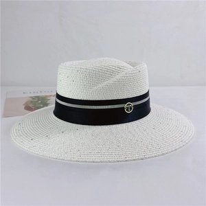 Detail view of a white woven straw sun hat featuring a black ribbon and metallic T logo