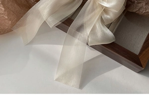 Close-up of beige organza ribbon bow hair clip with soft lighting on elegant background