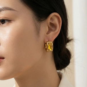 Detail view of a gold-plated chunky earring featuring a rectangular yellow gemstone inlay