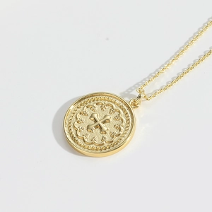 Macro detail of vintage gold coin pendant featuring a cross with lace edge on a thin chain