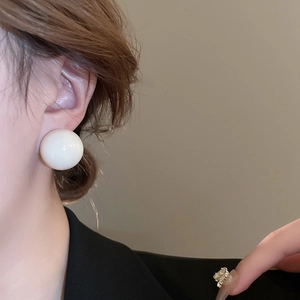 Close-up of a large white spherical stud earring on a model for a minimalist fashion look