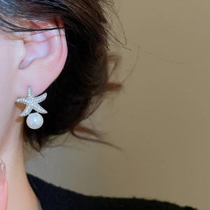 Gros plan sur les boucles d'oreilles perles et étoile de mer en argent sur l'oreille