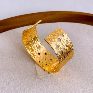 Primer plano de brazalete ancho dorado con textura plisada y recortes circulares de moda