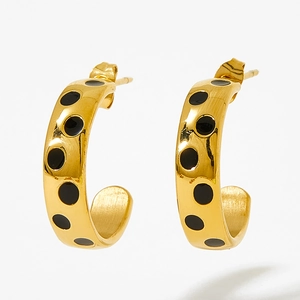 Gros plan de boucles d'oreilles créoles dorées avec pois en émail noir et métal poli