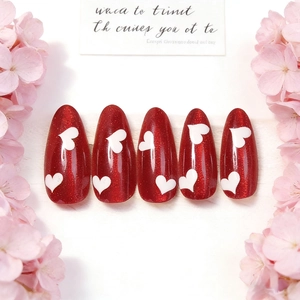 Cat eye red almond press-on nails with white heart patterns and glitter finish