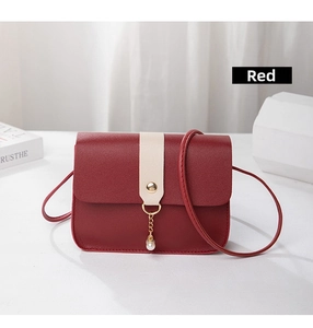 Detail of red leather crossbody bag featuring a golden buckle and elegant pearl charm