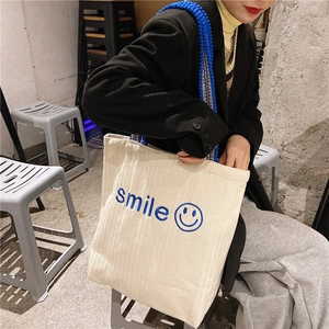 Detail of embroidered blue smile logo and textured blue strap on corduroy tote bag