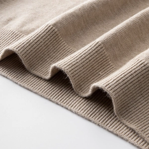 Detail eines haferfarbenen Strickpullovers mit feiner Textur und geripptem Saum am Armel