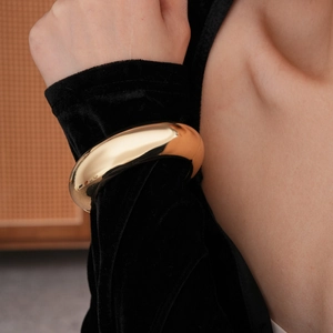 Close-up of a wide polished gold metal bangle featuring a chunky minimalist mirror finish
