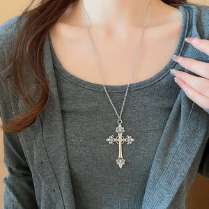Close-up of a silver vintage cross pendant necklace with diamonds worn by a model
