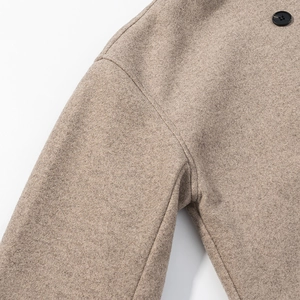 Detail view of beige wool coat featuring textured fabric and black button stitching