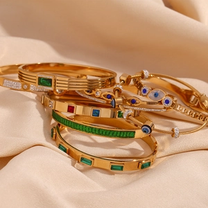 Close-up of 18K gold-plated bracelets featuring emerald gemstones and evil eye charms