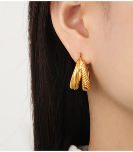 Close-up of gold-plated U-shaped earrings with smooth and ribbed texture on a model