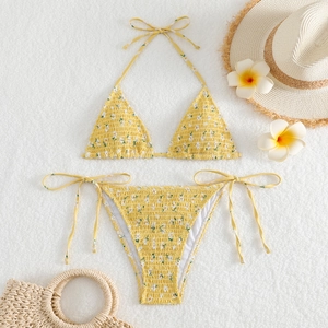 Flat lay of yellow floral smocked bikini set with beach accessories on white fur background