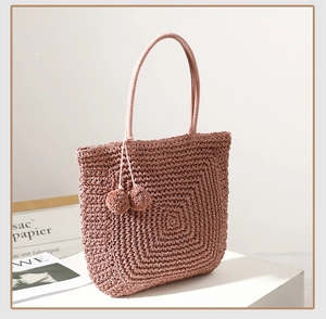 Detailed view of pink straw woven tote bag with matching pom-pom charms and spiral texture