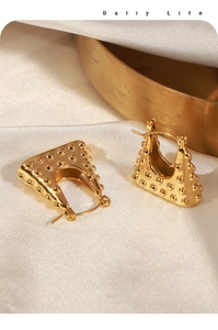 Detail of golden U-shaped earrings with unique polka dot texture on silk fabric