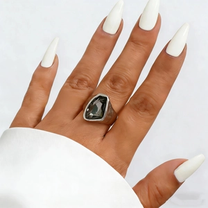 Detail of a geometric dark grey acrylic stone ring on a model with white manicured nails