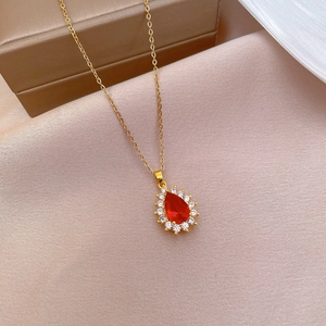 Close-up of a gold necklace featuring a pear-cut red gemstone with a sparkling halo setting