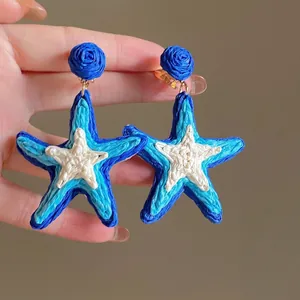 Detail of bohemian raffia starfish earrings with blue rose studs held by hand