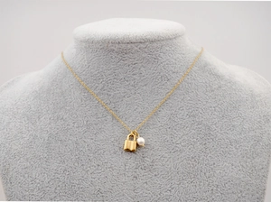 Détail d'un collier en titane doré avec un petit cadenas et un pendentif en perle ronde