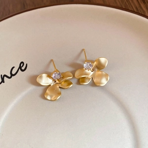 Detailed macro view of matte gold floral earrings with a central cubic zirconia stone
