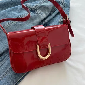 Close-up of red patent leather shoulder bag featuring a gold horseshoe buckle detail