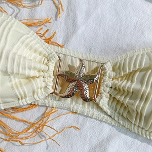 Macro view of a gold starfish buckle on creamy pleated bikini fabric with raffia detail