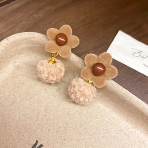 Close-up of brown flocked flower earrings with soft pom-poms and pearl accents