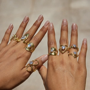 Detalle de anillos de acero dorado con texto Mom y circonitas en forma de corazón fino
