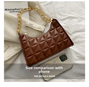 Detailed view of brown quilted crescent bag with gold chain strap next to smartphone