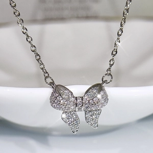 Sparkling silver bow pendant necklace with micro-paved crystals on white porcelain edge