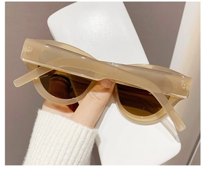 Detailed close-up of retro cat-eye sunglasses in milk tea beige finish held by hand