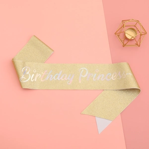 Close-up of golden glitter birthday princess sash on a soft pink paper background