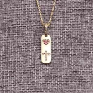Minimalist gold-plated necklace with pink heart and white cross pendant on grey background