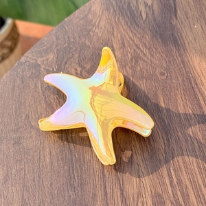 Iridescent starfish hair claw clip with holographic finish on dark wood background