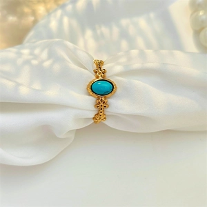 Detail of vintage gold ring with oval turquoise stone on white silk background
