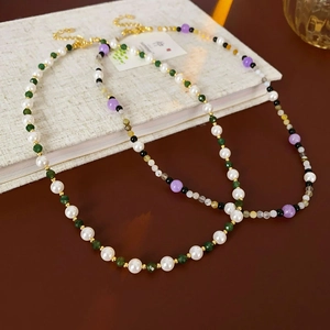 Detail of beaded necklace with pearls, green and purple beads, and gold lobster clasp