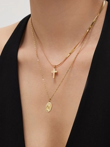 Close-up of layered gold necklaces with zircon cross and oval icon pendant on a model