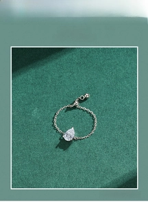 Close-up of adjustable silver chain ring featuring a teardrop zirconia on green backdrop