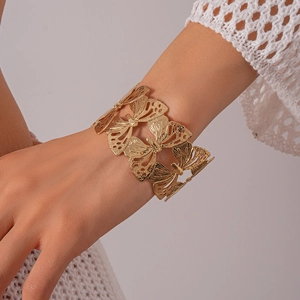 Detailed view of wide open cuff bracelet with intricate hollow gold butterfly patterns