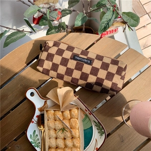 Flat lay of brown checkerboard corduroy pencil case on wooden table in sunlight