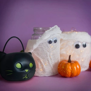 Detail of Halloween ghost jars with LED lights and black cat bucket on purple background